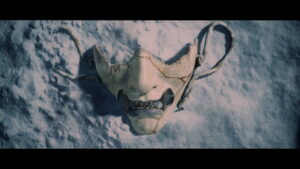A cracked samurai mask lying on snow in Ghost of Yotei