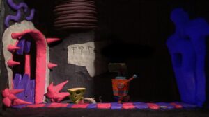 The claymation protagonist Klaymen stands beside a spiked pink door and a piece of cheese in The Neverhood.
